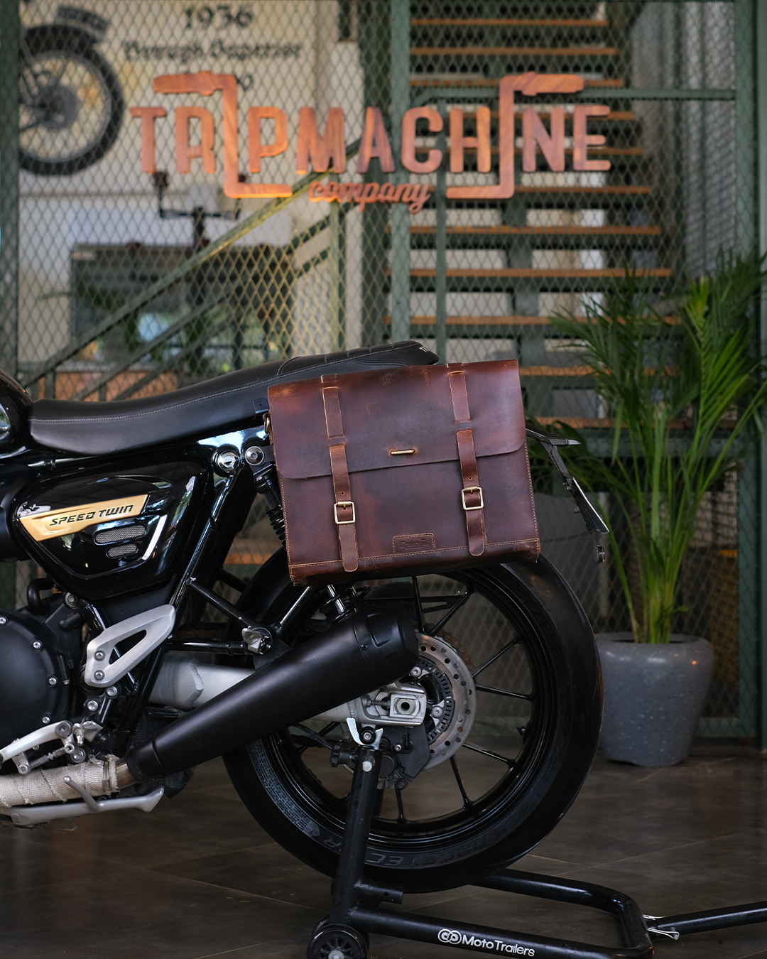 Motorcycle with a brown leather saddlebag in front of a 'Trip Machine' sign.