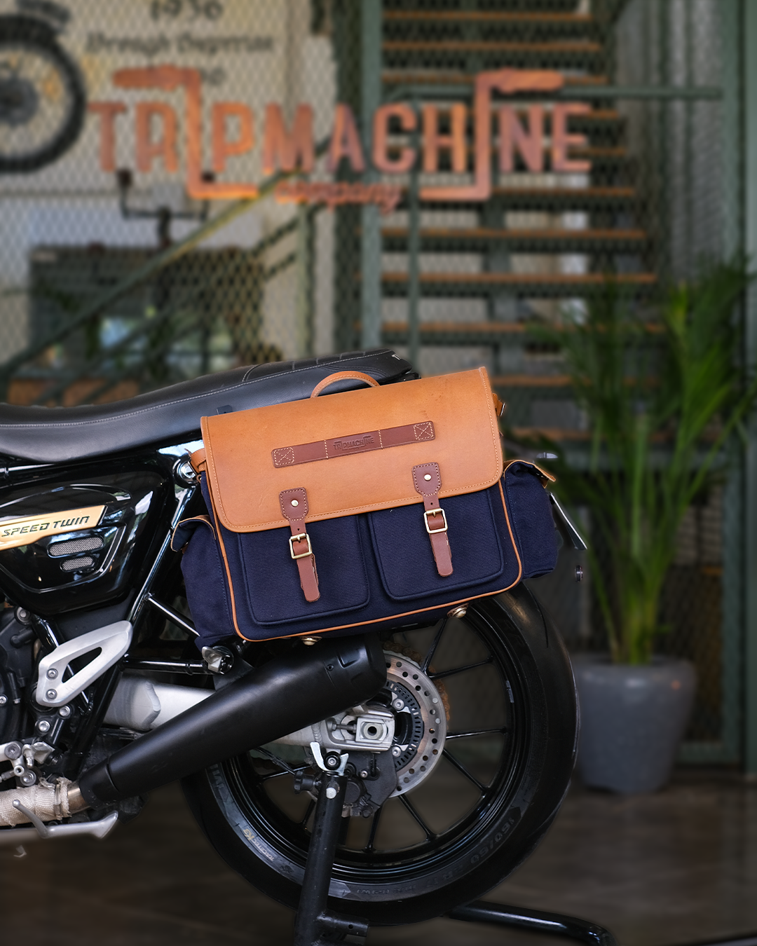 Motorcycle with a brown and blue saddlebag in front of a 'Tap Machine' sign.