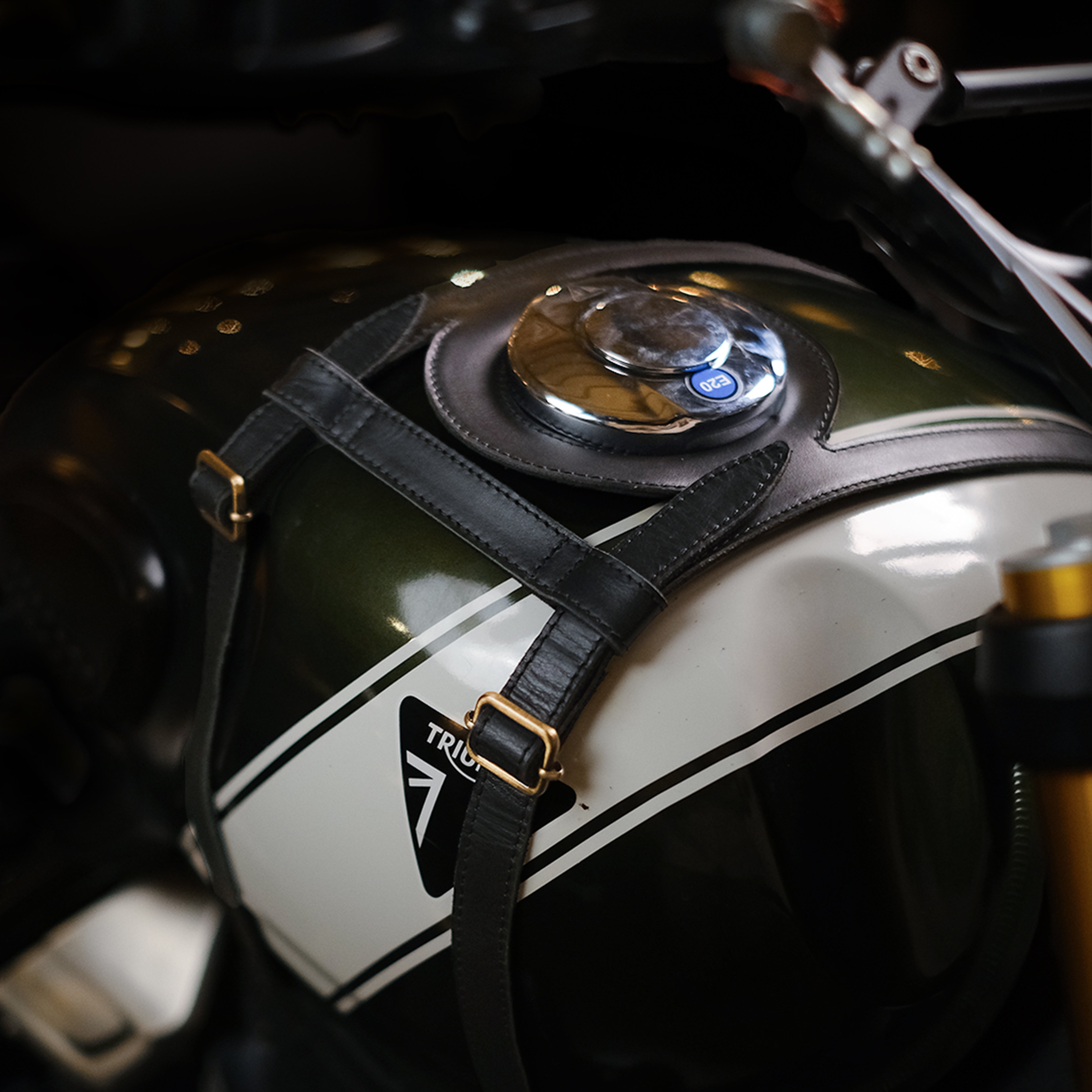 Close-up of a motorcycle fuel tank with a helmet strap and 'Triumph' logo.