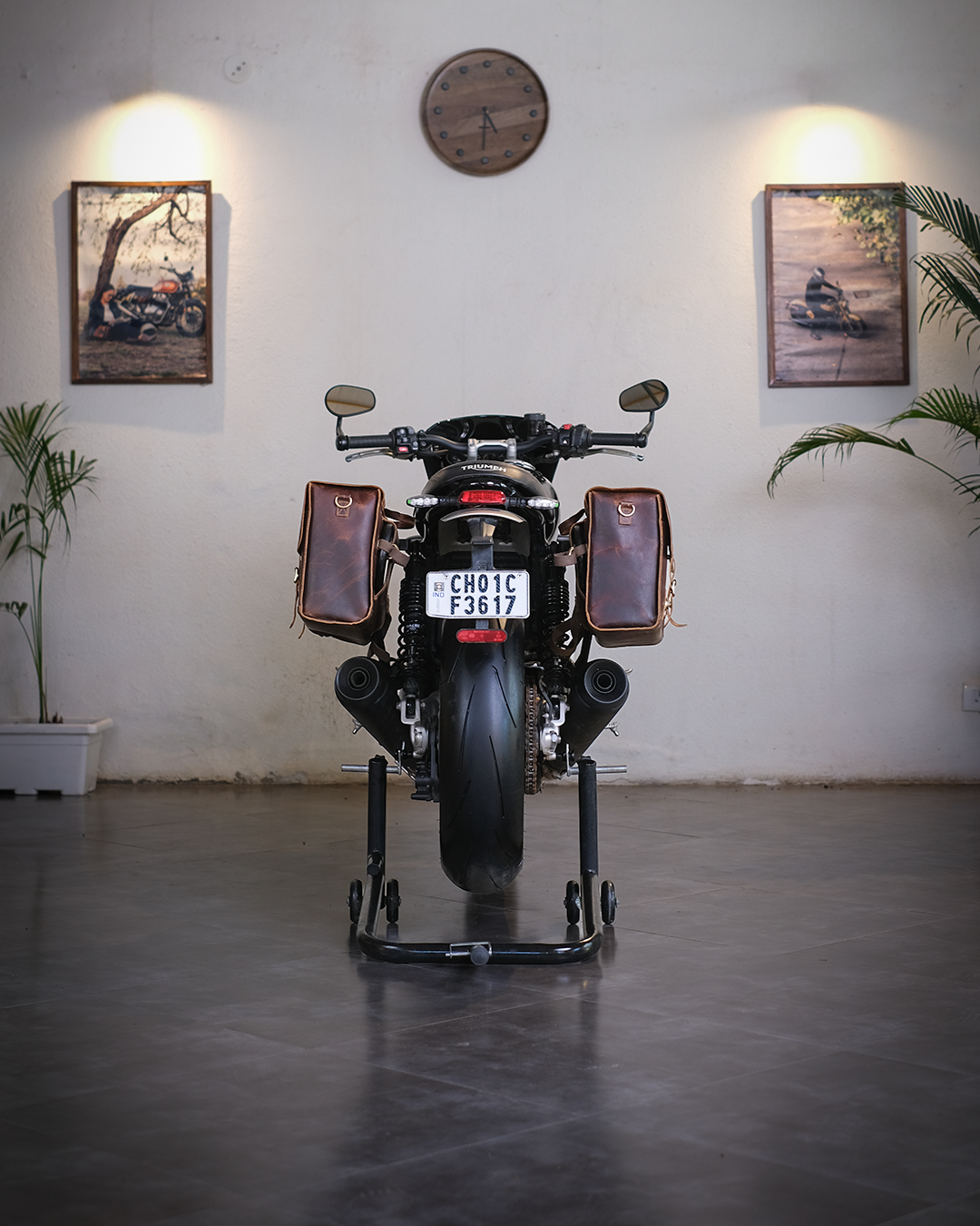 Motorcycle on a stand in a room with framed pictures and a clock on the wall.