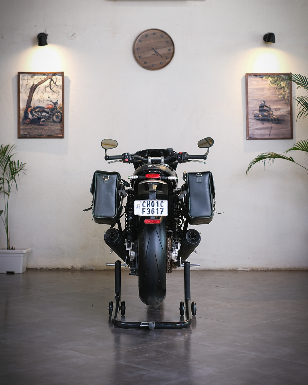 Motorcycle on a stand in a room with a clock and framed pictures on the wall.