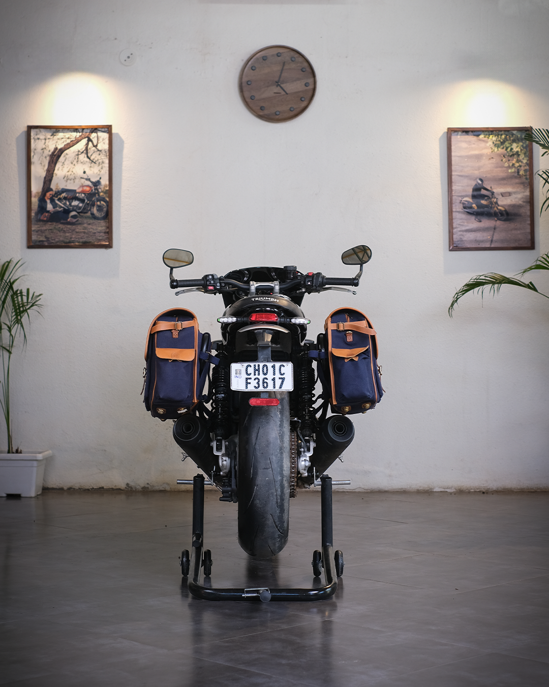 Motorcycle with saddlebags on a stand against a white wall with framed pictures and a clock.