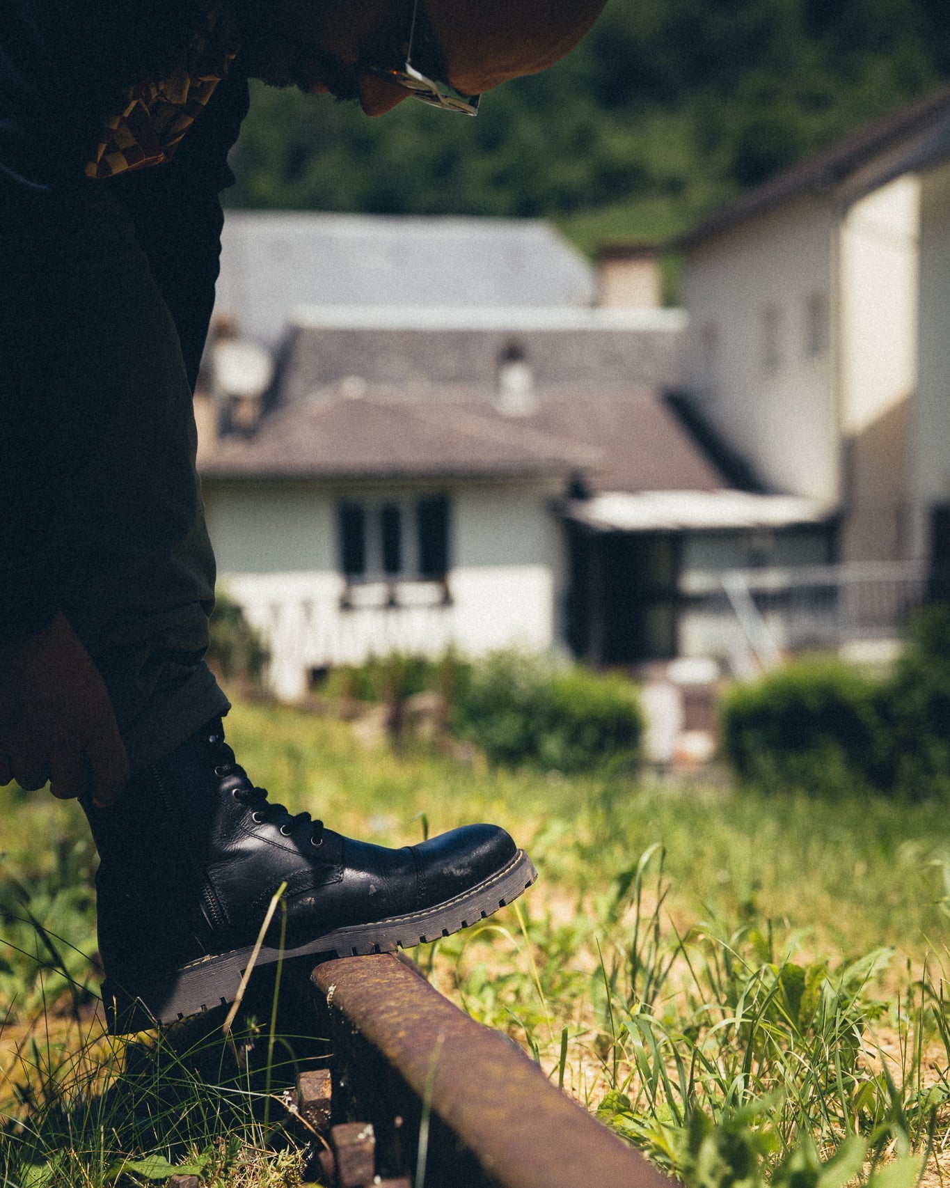 Person wearing black boots stepping onto a railway track with houses in the background