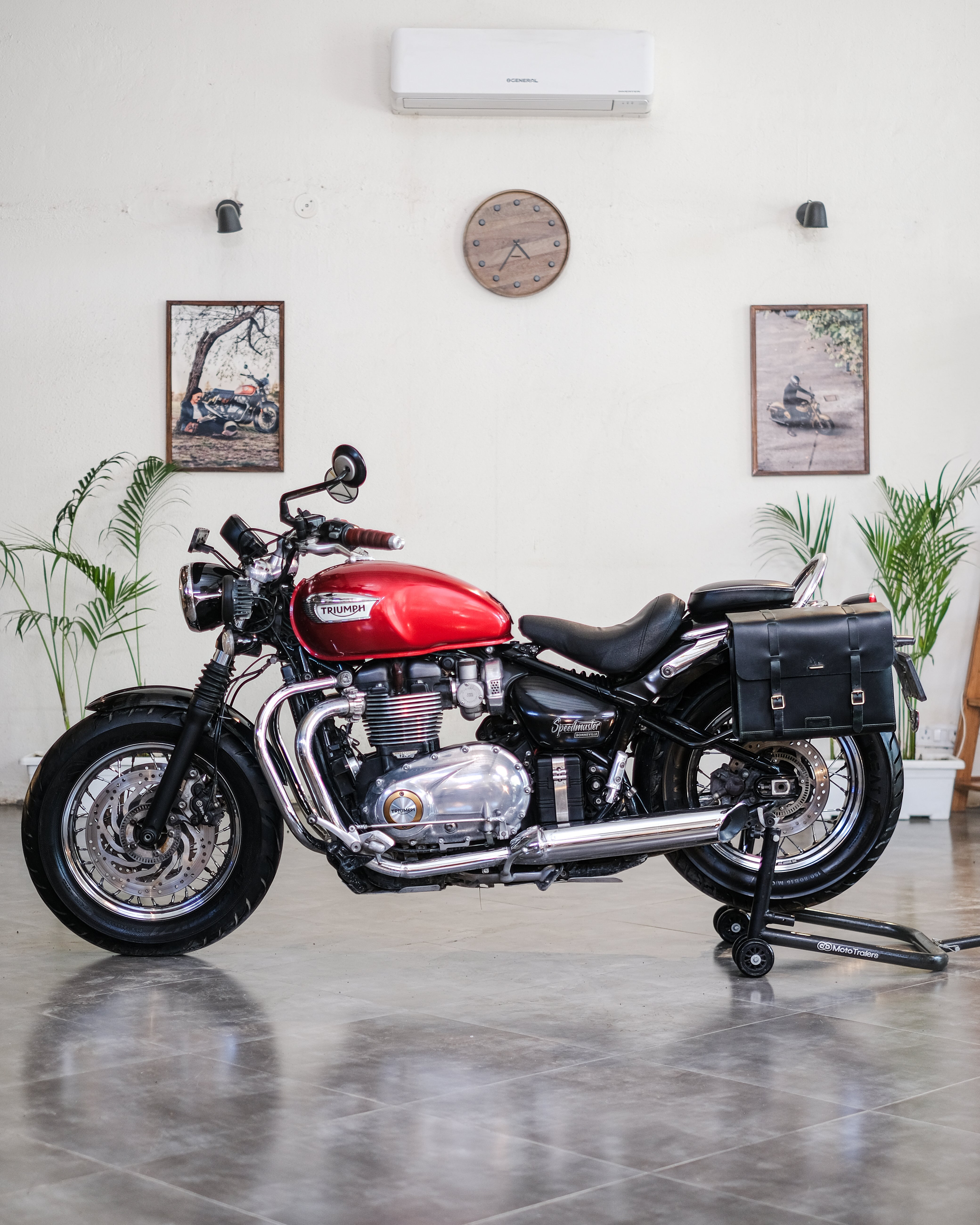 Red and black motorcycle indoors with a white wall and plants in the background