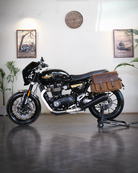 Black motorcycle with a brown bag on a stand in a room with plants and framed pictures.