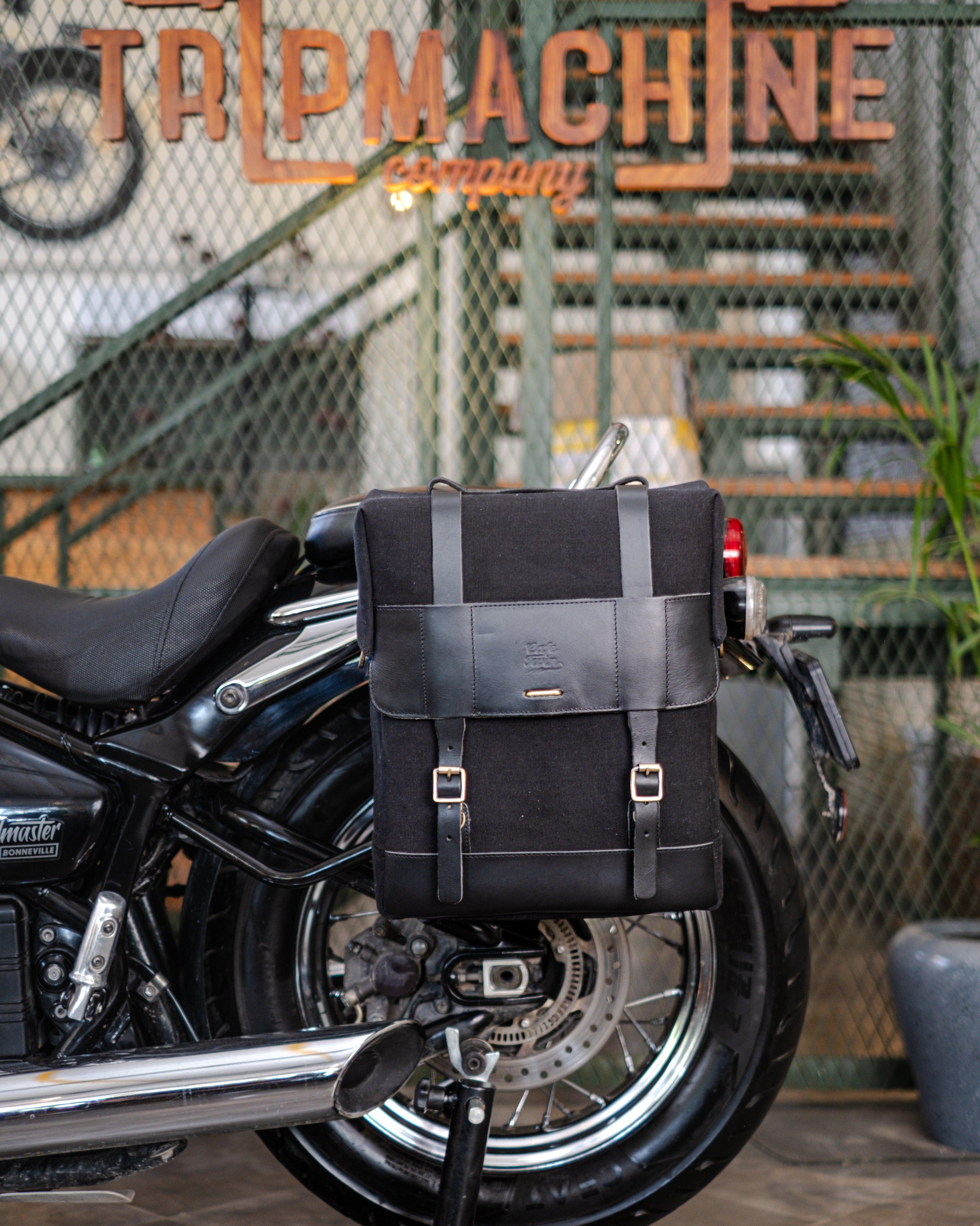 Motorcycle with black saddlebags in front of a metal fence with 'TRIPMACHINE' branding.