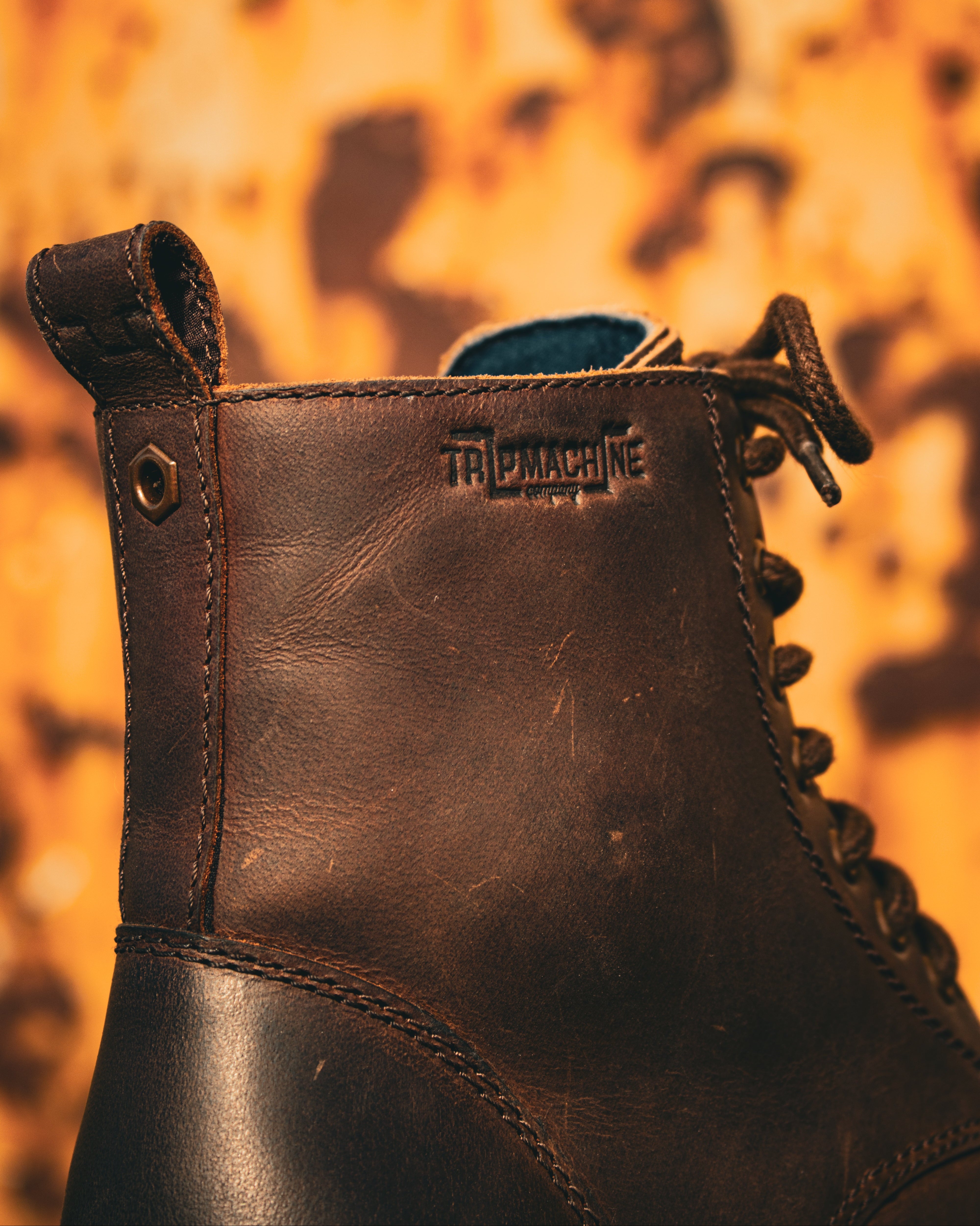 Brown leather boot with 'Triple Machine' branding against a blurred background