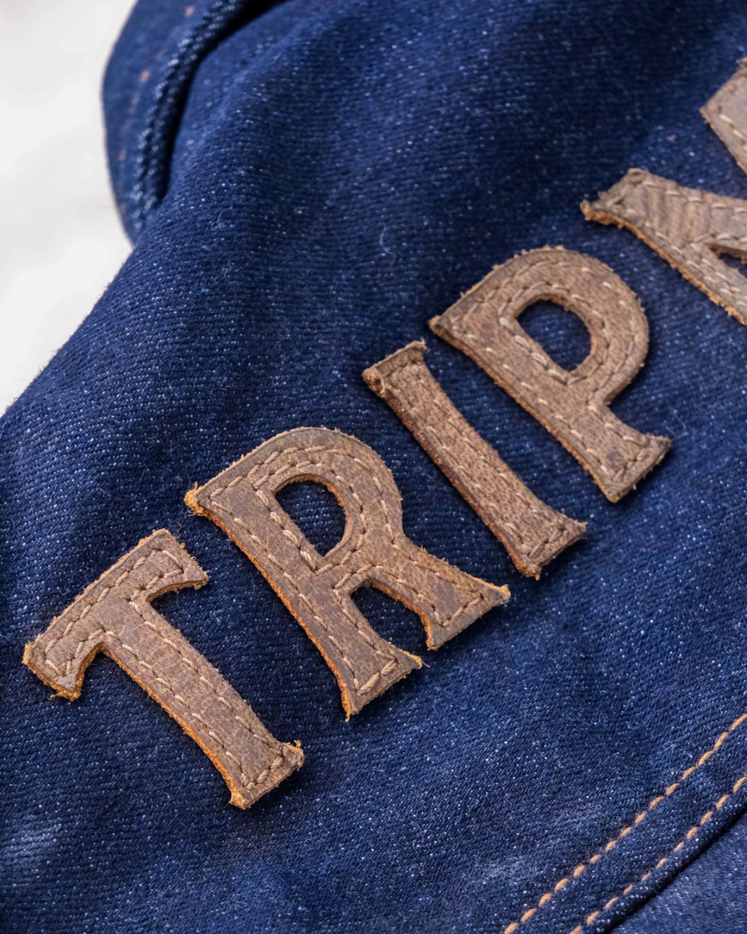 Close-up of a blue denim jacket with 'TRIP' embroidered in brown letters.